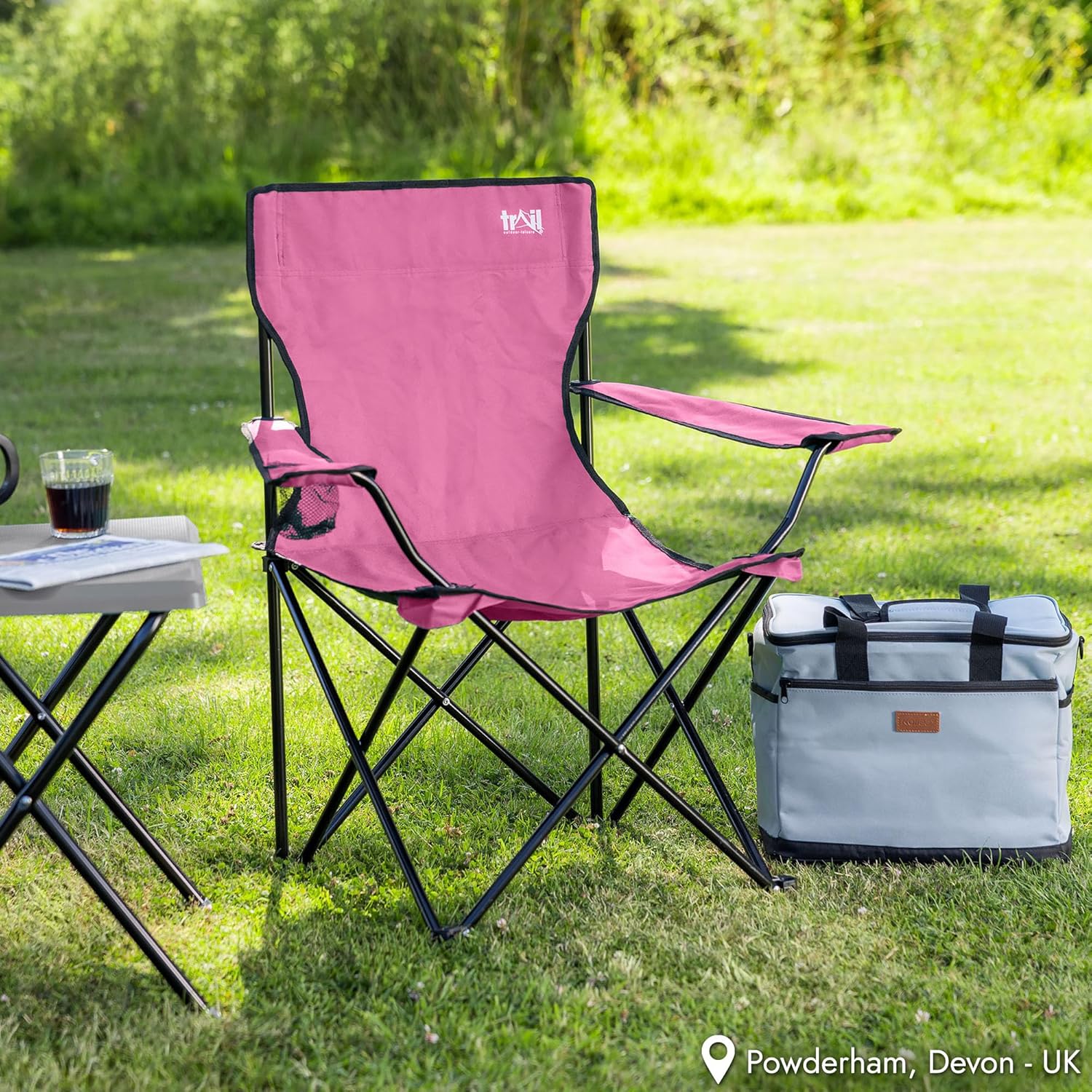 Pink Trail folding chair set up on a lawn beside a small camping table and cool bag