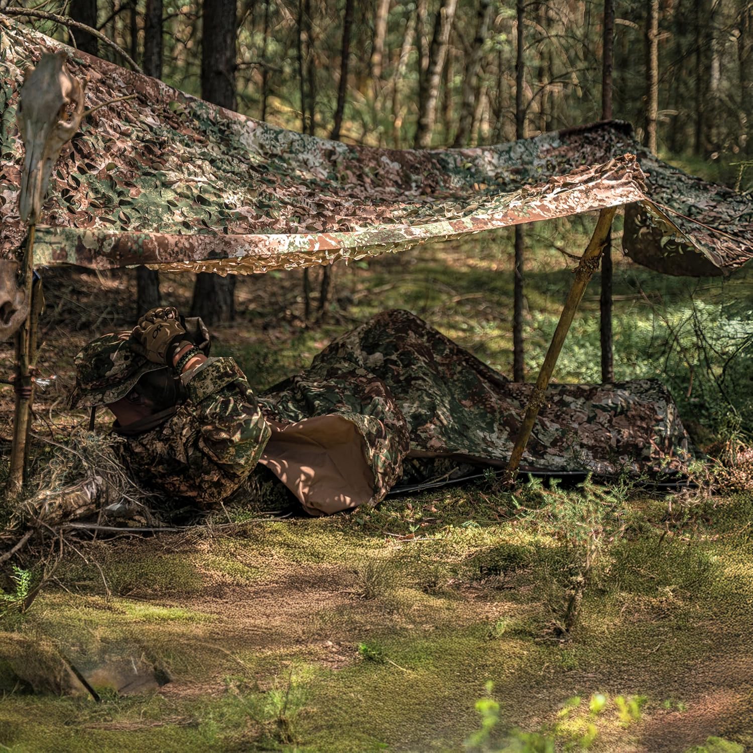 Camper zipped into the Mil-Tec bivvy cover lying under a camouflage net tarp in woodland