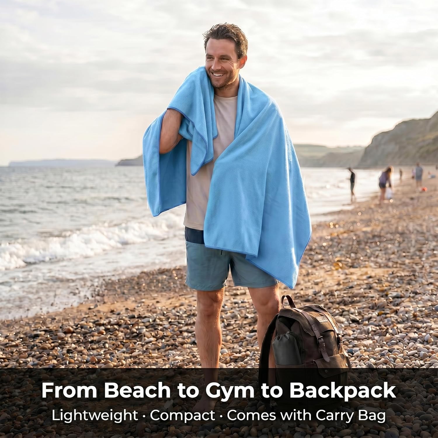Camper on a UK beach with the blue HomlyPro microfibre towel draped over his shoulders next to a backpack
