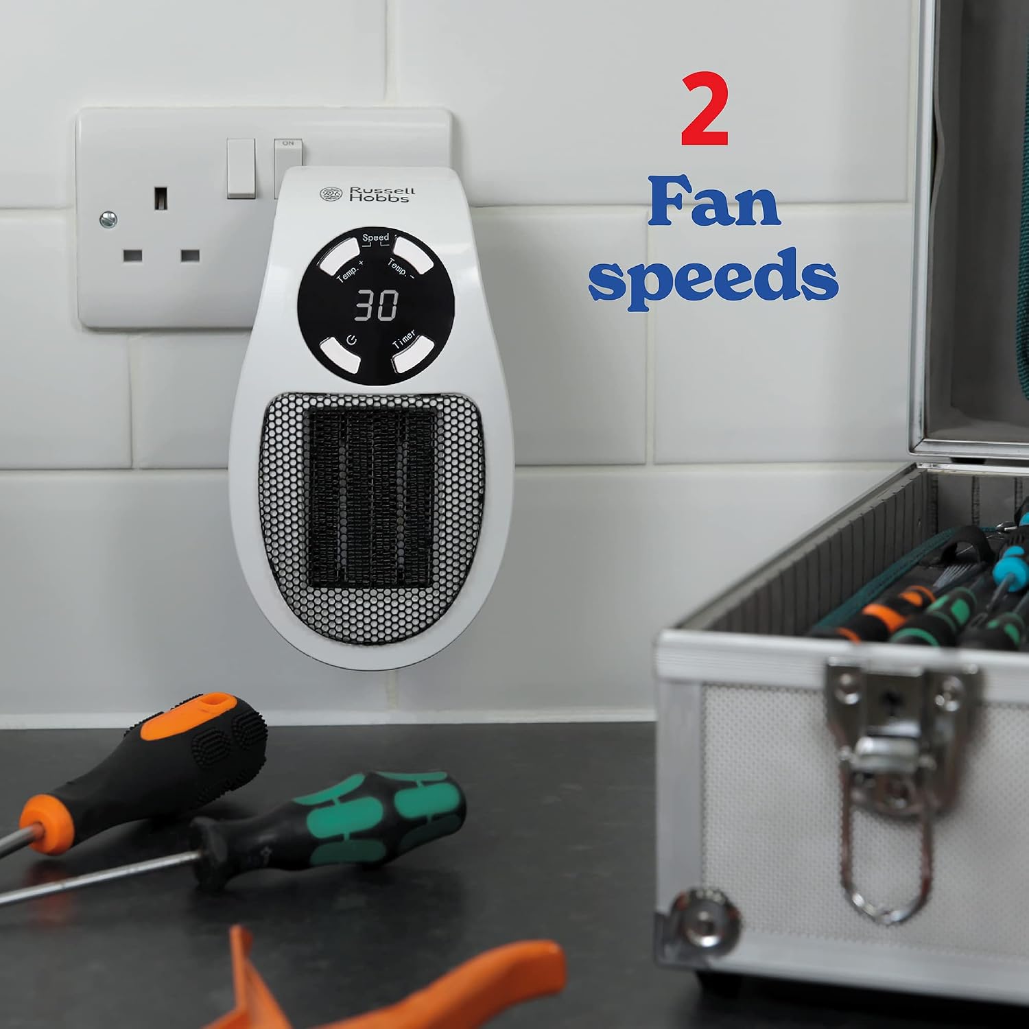 The plug heater hanging from a double socket above a workbench with screwdrivers and an open tool case, captioned 2 fan speeds