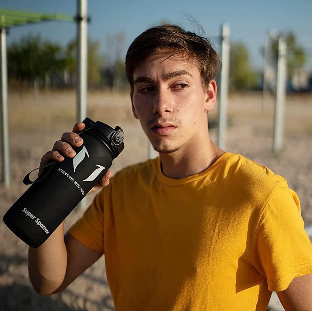 Man drinking from a black Super Sparrow bottle at an outdoor exercise park