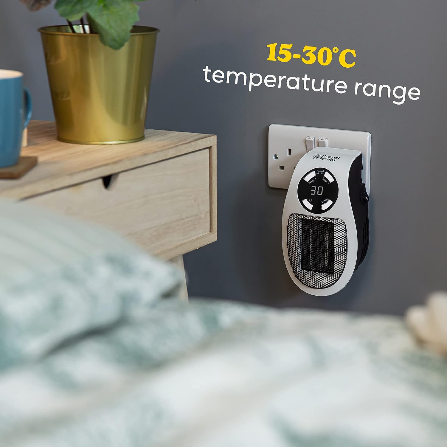 The heater plugged in beside a bed and a wooden bedside table, captioned 15-30C temperature range