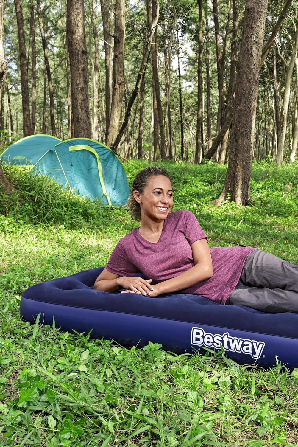 Woman lying on the Bestway single air bed on grass in front of a green camping tent, smiling