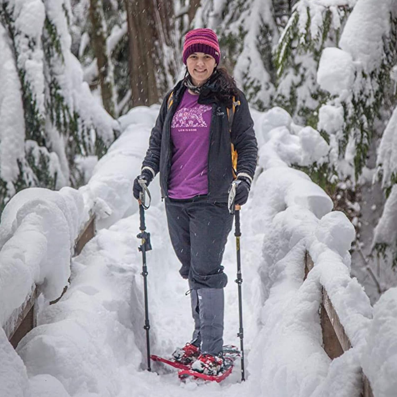 Walker in gaiters and snowshoes crossing a snow-covered wooden footbridge