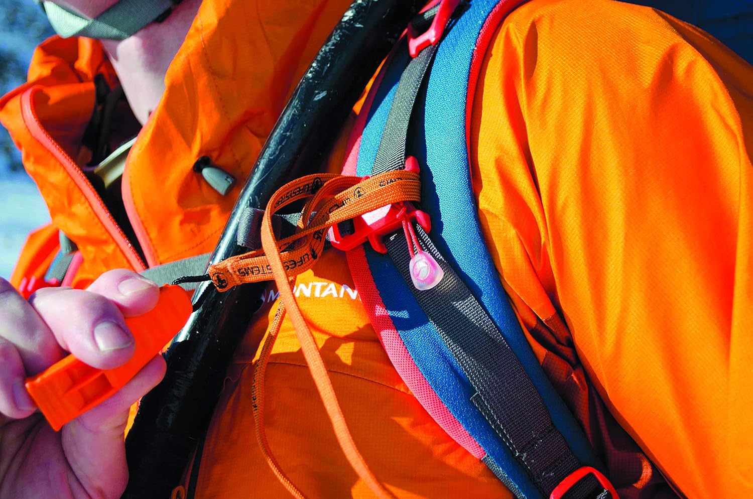 Lifesystems emergency whistle clipped to an orange backpack chest strap alongside other outdoor gear