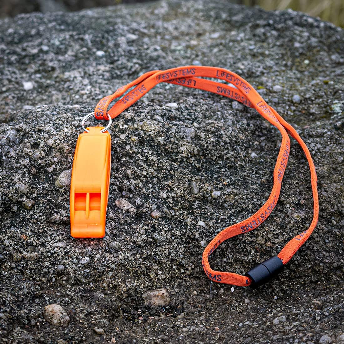 Lifesystems emergency whistle with full lanyard laid out on grey rock surface outdoors