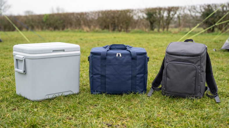 Hard cool box, soft cool bag and cooler rucksack compared side by side on campsite grass