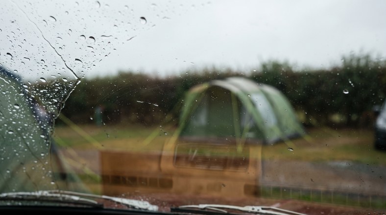 Rain running down a car windscreen at a wet UK campsite while deciding whether to camp in the rain