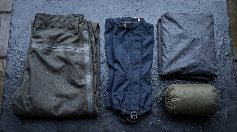 Waterproof over trousers, gaiters and a rain poncho laid out wet for camping in the rain in the UK