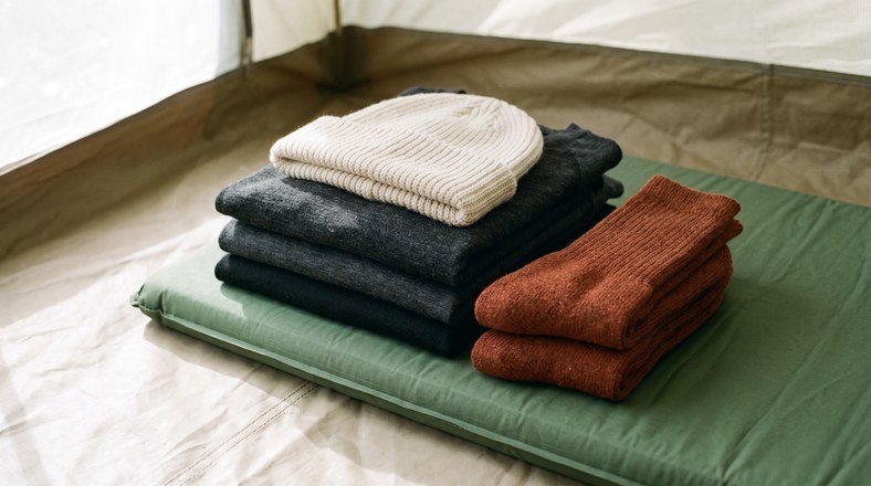 Folded merino base layers, wool socks and a beanie for layering up to stay warm in a tent
