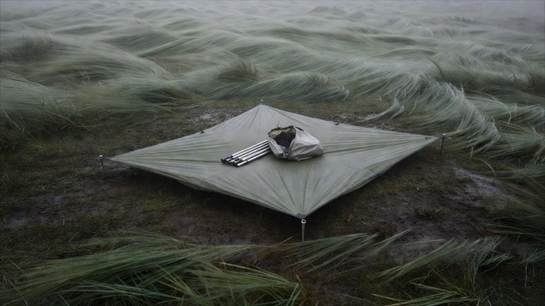 Collapsed tent pinned at its windward corners while striking camp in wind