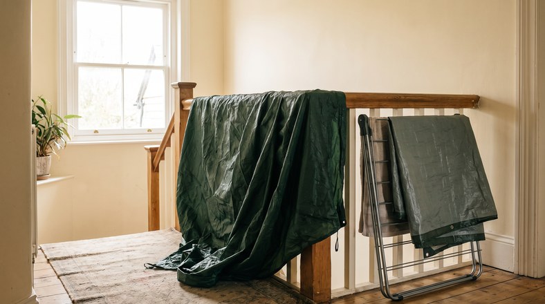 Wet tent flysheet drying over a bannister indoors after a rainy UK camping trip